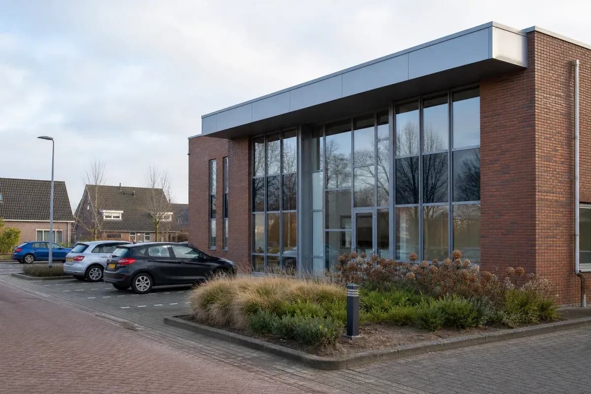 Modern kantoorpand met parkeerterrein overdag.