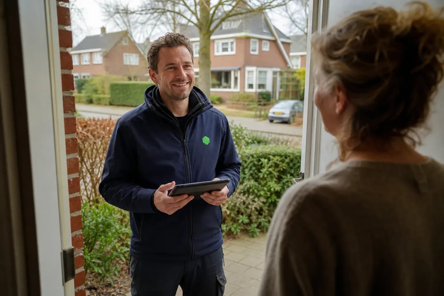 Vakman met tablet in de hand praat glimlachend met een bewoner bij de voordeur.